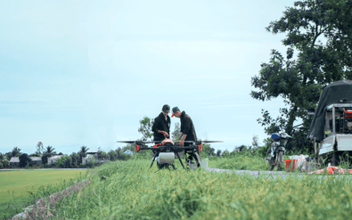 Drone pilots preparing the drone by rice paddy for fertilizer spreading
